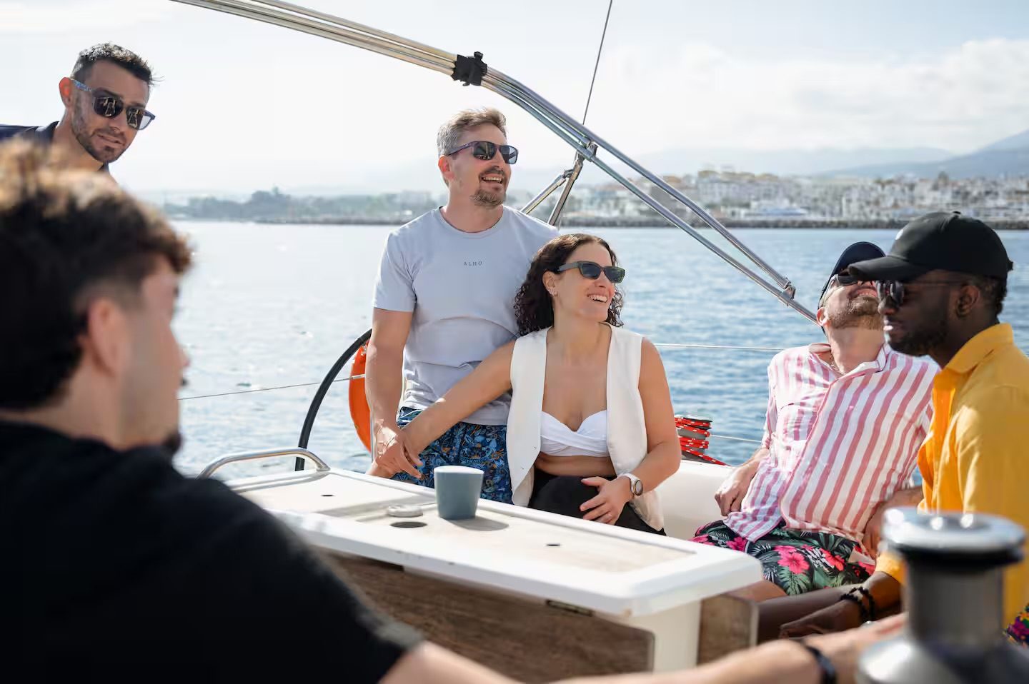 Grupo de amigos disfrutando a bordo de un chárter privado de velero en Marbella, con Puerto Banús al fondo