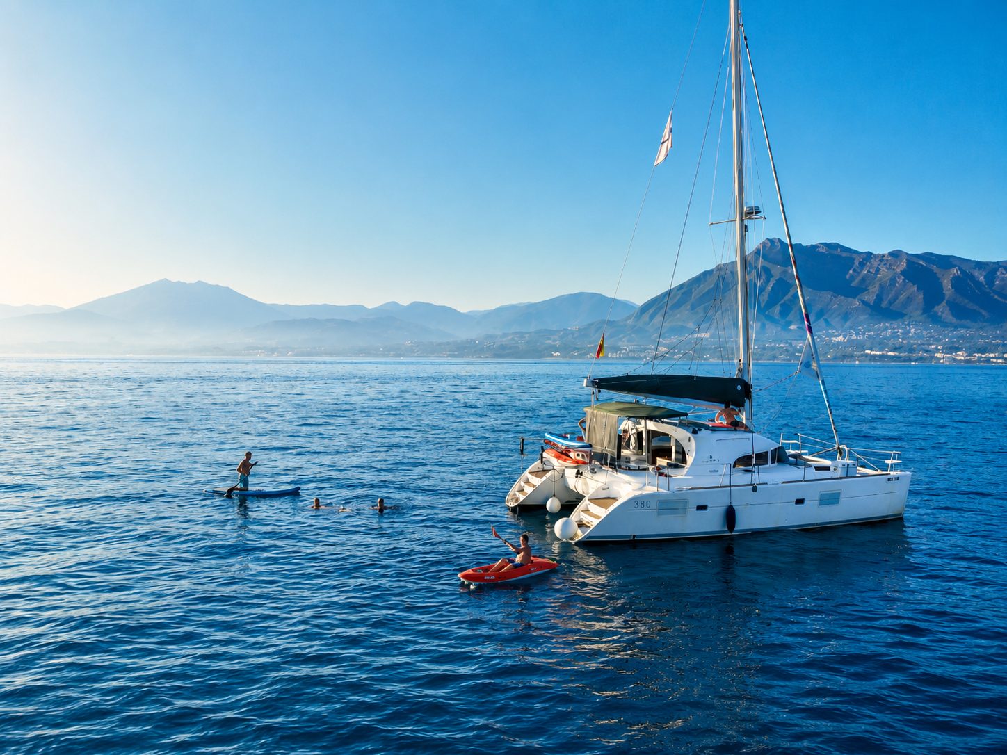 Catamaran anchored off Marbella with guests paddleboarding and swimming on a swim stop